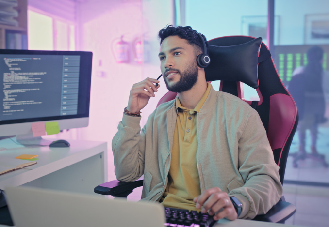 Un technicien d'assistance en informatique devant son écran d'ordinateur. Il porte un micro casques et est en train de répondre à la demande d'un client qui a besoin d'une aide informatique